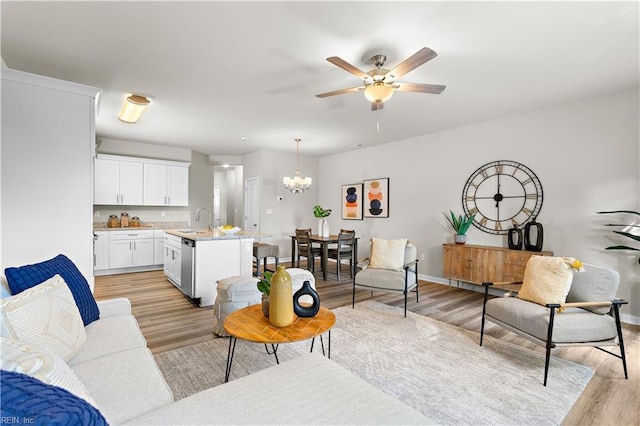 living room with ceiling fan with notable chandelier, light hardwood / wood-style flooring, and sink