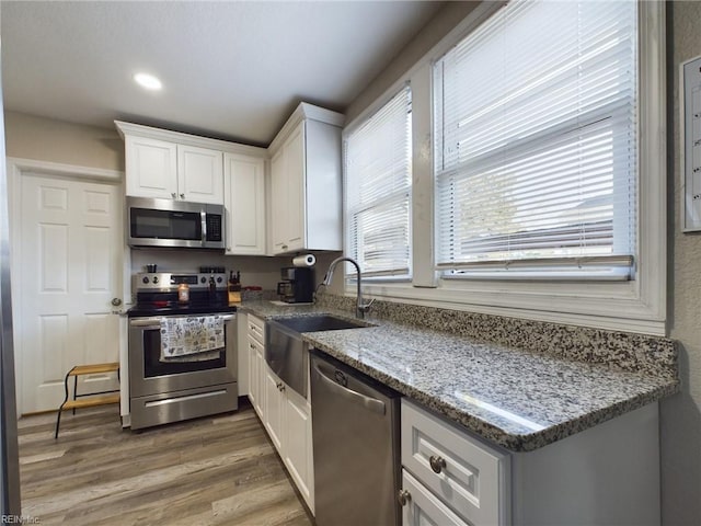 kitchen with white cabinetry, sink, dark wood-type flooring, stainless steel appliances, and light stone counters