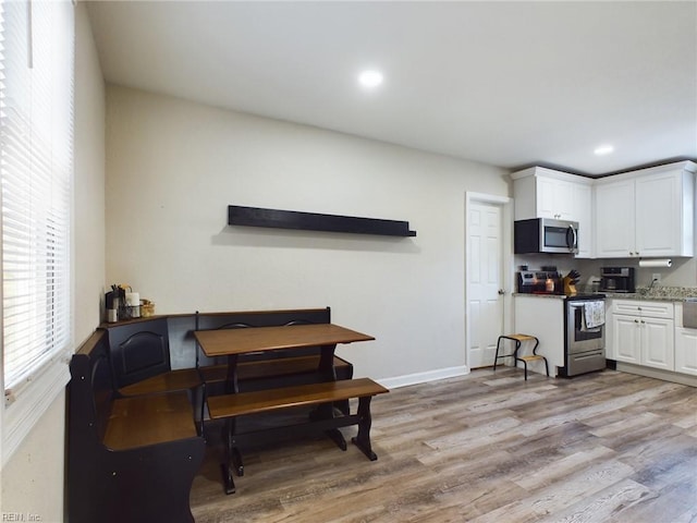 kitchen with light stone countertops, white cabinets, light wood-type flooring, and appliances with stainless steel finishes