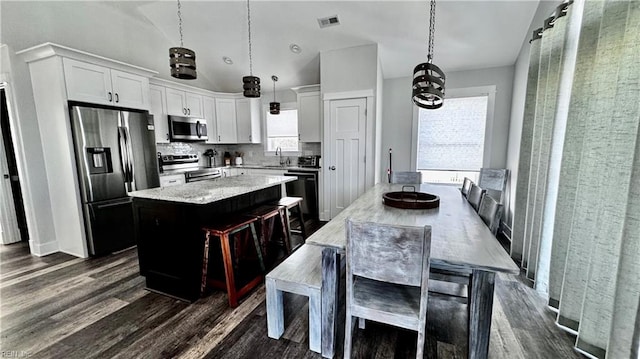 kitchen featuring appliances with stainless steel finishes, a center island, decorative light fixtures, and white cabinetry