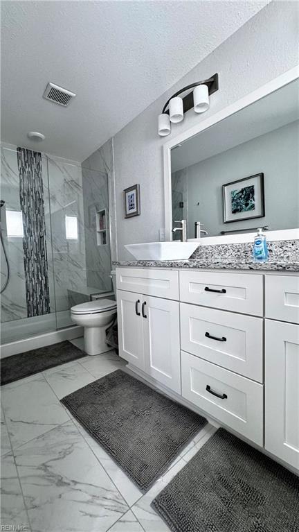 bathroom with tiled shower, a textured ceiling, vanity, and toilet