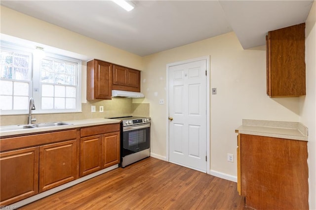 kitchen featuring backsplash, stainless steel electric range oven, sink, and wood-type flooring