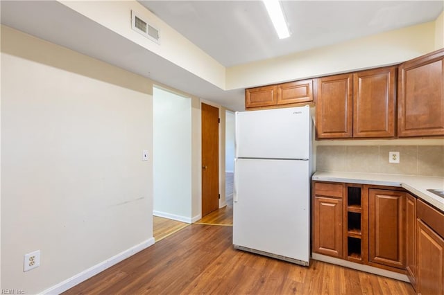 kitchen featuring white refrigerator, light wood-type flooring, and tasteful backsplash