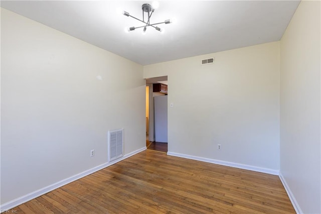 empty room with hardwood / wood-style flooring and an inviting chandelier