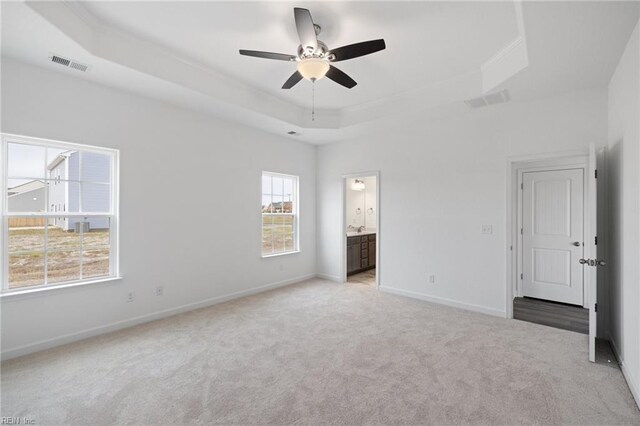 unfurnished bedroom featuring light carpet, a tray ceiling, ensuite bath, and ceiling fan