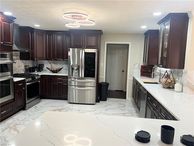 kitchen featuring light stone countertops, sink, stainless steel appliances, wall chimney range hood, and backsplash