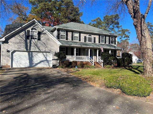 colonial-style house featuring covered porch, a garage, and a front yard