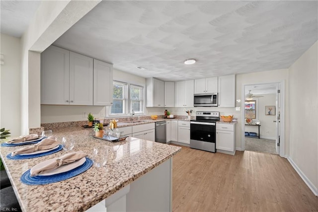 kitchen featuring kitchen peninsula, white cabinets, stainless steel appliances, and light hardwood / wood-style floors