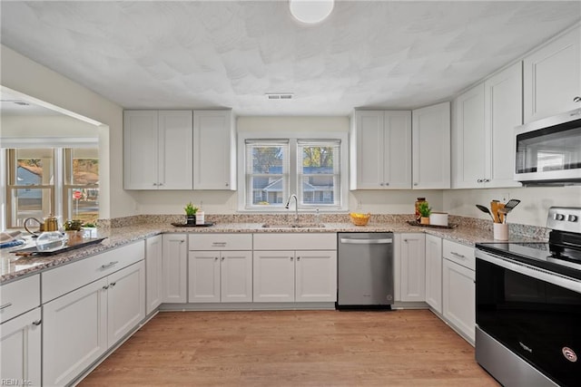 kitchen with appliances with stainless steel finishes, light wood-type flooring, light stone counters, sink, and white cabinetry