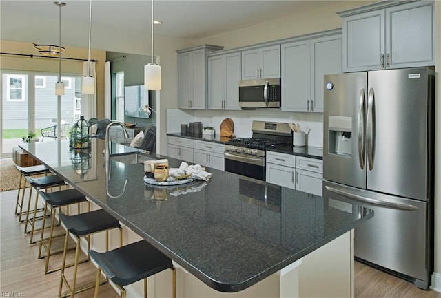 kitchen featuring appliances with stainless steel finishes, light hardwood / wood-style flooring, dark stone counters, and an island with sink