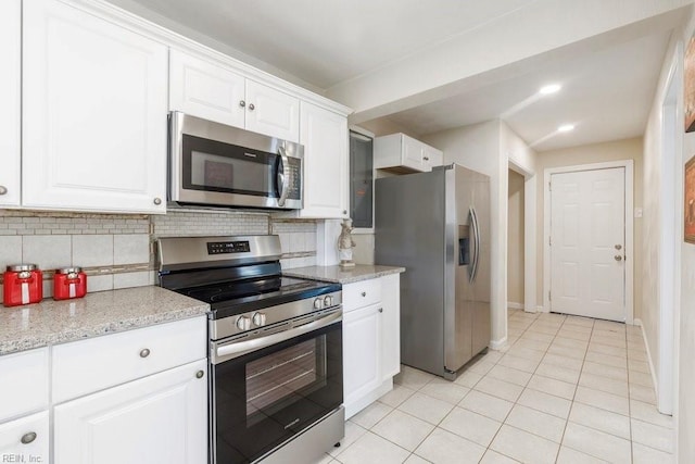 kitchen featuring light stone countertops, backsplash, stainless steel appliances, white cabinetry, and light tile patterned flooring