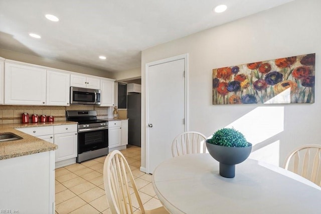 kitchen with sink, decorative backsplash, light tile patterned flooring, white cabinetry, and stainless steel appliances