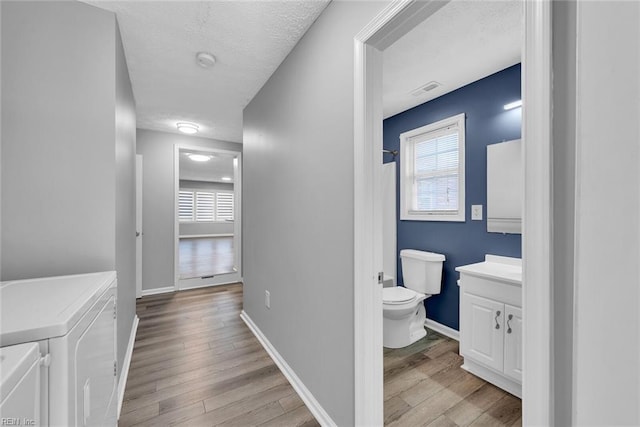 bathroom with independent washer and dryer, a textured ceiling, toilet, vanity, and hardwood / wood-style flooring