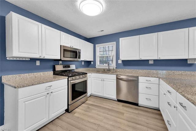 kitchen featuring sink, stainless steel appliances, a textured ceiling, white cabinets, and light wood-type flooring