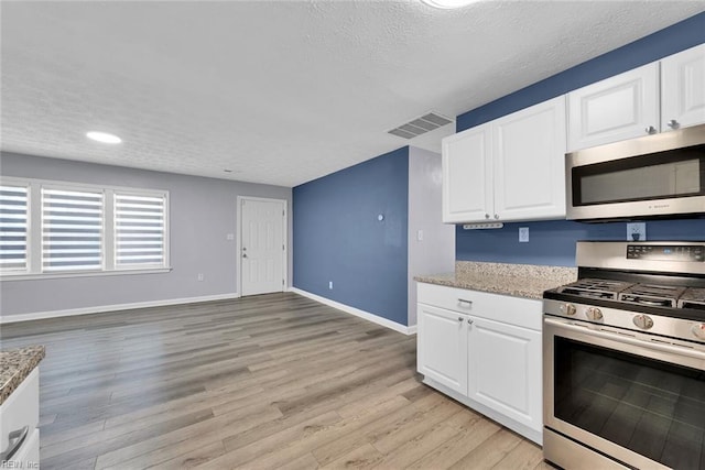 kitchen with a textured ceiling, white cabinetry, stainless steel appliances, and light hardwood / wood-style flooring