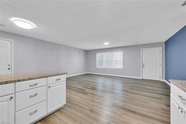 kitchen with light stone countertops, light wood-type flooring, white cabinetry, and a textured ceiling