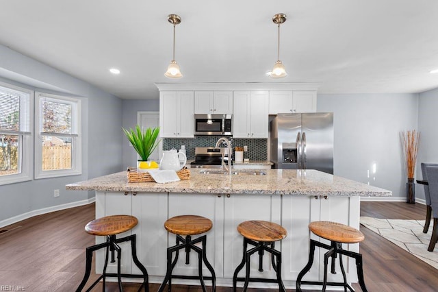 kitchen featuring white cabinetry, stainless steel appliances, dark hardwood / wood-style flooring, pendant lighting, and a kitchen island with sink