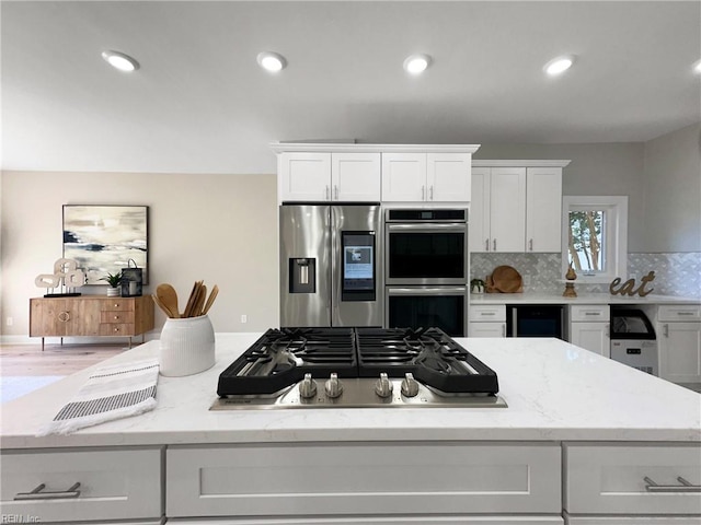 kitchen with light stone counters, backsplash, hardwood / wood-style floors, white cabinets, and appliances with stainless steel finishes