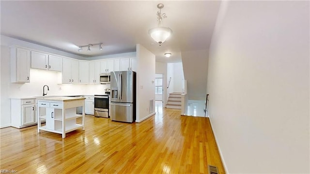 kitchen featuring sink, hanging light fixtures, light hardwood / wood-style floors, white cabinetry, and stainless steel appliances