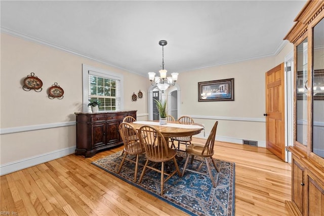 dining area with light hardwood / wood-style floors, an inviting chandelier, and crown molding