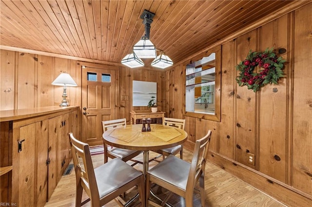 dining space featuring light hardwood / wood-style floors, wood ceiling, ornamental molding, and wooden walls