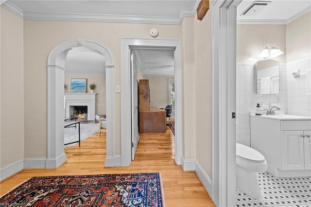 hallway with crown molding, light hardwood / wood-style flooring, tile walls, and sink