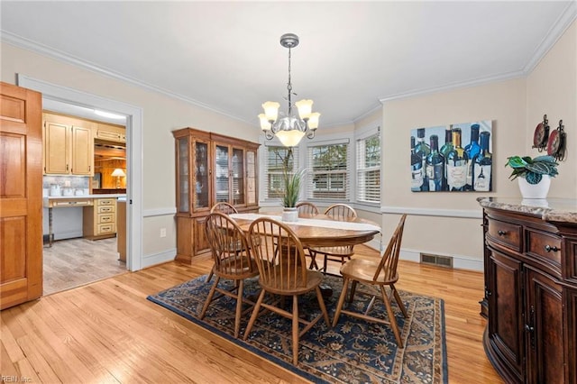 dining space featuring light wood-type flooring, ornamental molding, and a notable chandelier