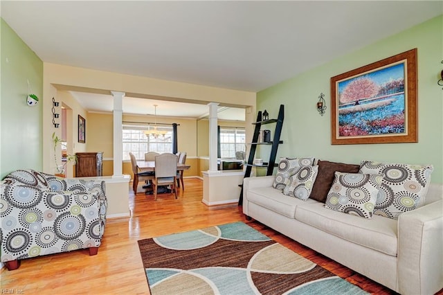 living room featuring an inviting chandelier, light wood-type flooring, and decorative columns