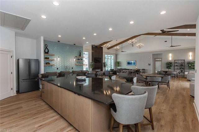 kitchen with high quality fridge, a large island, light wood-type flooring, and vaulted ceiling with beams