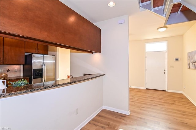 kitchen with dark stone counters, kitchen peninsula, stainless steel fridge, and light hardwood / wood-style floors