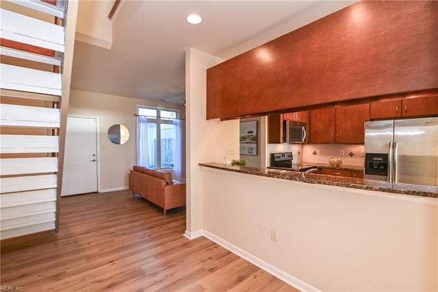 kitchen featuring backsplash, dark stone counters, light hardwood / wood-style flooring, appliances with stainless steel finishes, and kitchen peninsula