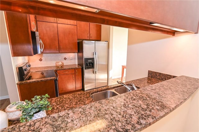 kitchen with kitchen peninsula, sink, dark stone counters, and appliances with stainless steel finishes