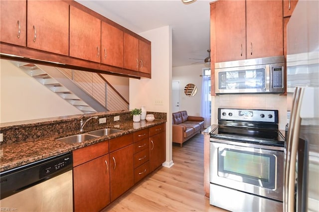 kitchen featuring sink, ceiling fan, dark stone countertops, appliances with stainless steel finishes, and light hardwood / wood-style floors