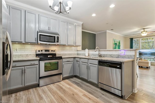 kitchen with kitchen peninsula, light wood-type flooring, stainless steel appliances, sink, and decorative light fixtures