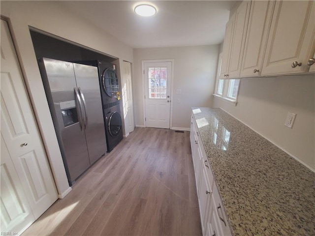 kitchen featuring stainless steel fridge with ice dispenser, light stone counters, white cabinets, stacked washer and clothes dryer, and light wood-type flooring