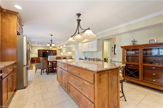 kitchen featuring light stone counters, a breakfast bar, pendant lighting, a kitchen island, and stainless steel refrigerator