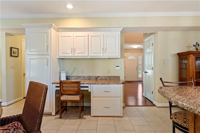 kitchen with light tile patterned floors, built in desk, white cabinetry, and light stone counters