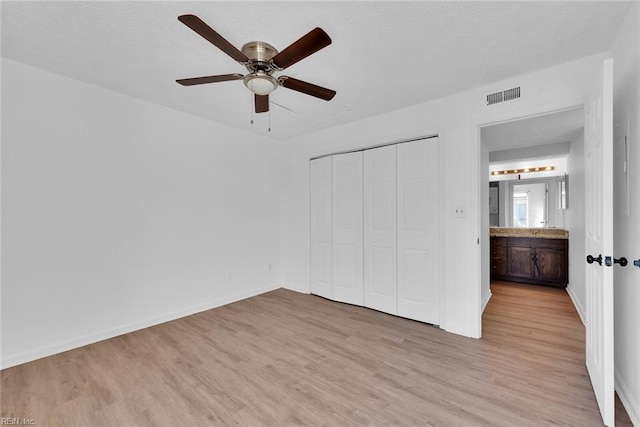 unfurnished bedroom with ceiling fan, light wood-type flooring, ensuite bathroom, and a closet