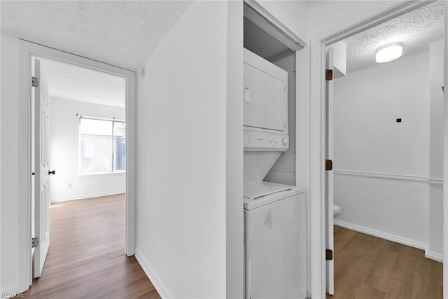 washroom with light hardwood / wood-style flooring, stacked washing maching and dryer, and a textured ceiling