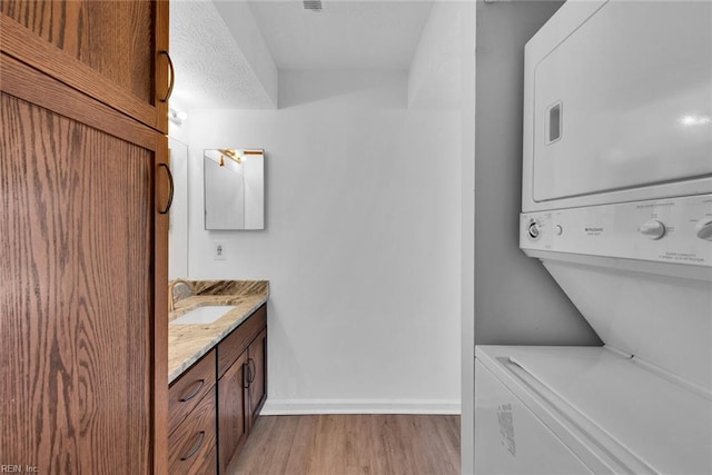 laundry area with a textured ceiling, light hardwood / wood-style floors, sink, and stacked washer and dryer