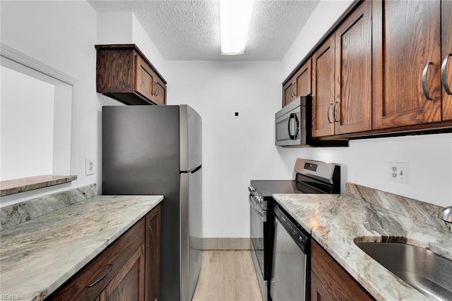 kitchen with light stone countertops, appliances with stainless steel finishes, a textured ceiling, sink, and light hardwood / wood-style flooring