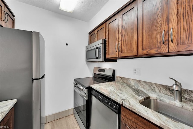 kitchen featuring sink, light wood-type flooring, a textured ceiling, light stone countertops, and appliances with stainless steel finishes