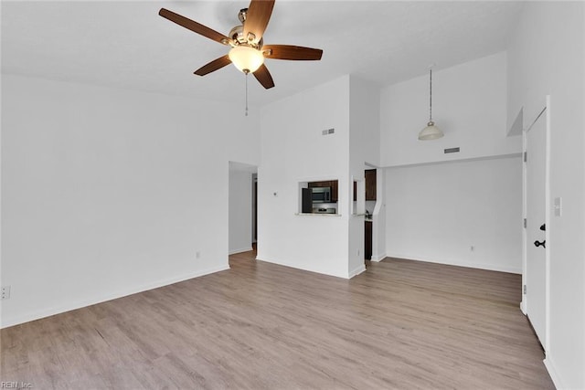 unfurnished living room featuring ceiling fan, a towering ceiling, and light hardwood / wood-style flooring