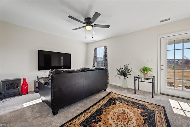 carpeted living room with a wood stove, ceiling fan, and a healthy amount of sunlight