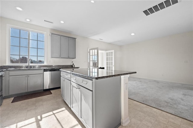 kitchen with light carpet, appliances with stainless steel finishes, dark stone counters, a center island, and gray cabinets