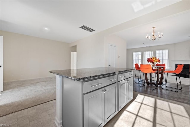 kitchen featuring pendant lighting, a center island, dark carpet, dark stone countertops, and a notable chandelier