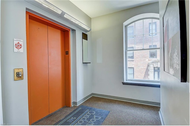 hall with dark colored carpet and elevator