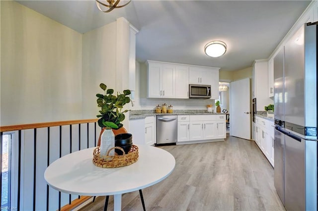 kitchen featuring white cabinets, light wood-type flooring, stainless steel appliances, and light stone counters