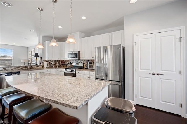 kitchen featuring light stone counters, a kitchen bar, hanging light fixtures, and appliances with stainless steel finishes