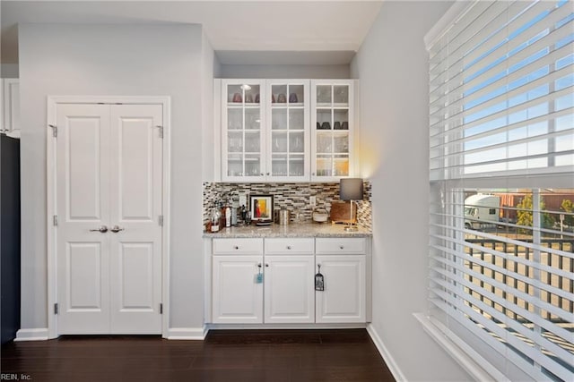 bar featuring black fridge, decorative backsplash, light stone counters, dark hardwood / wood-style flooring, and white cabinetry